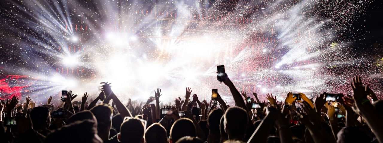 Lit up stage at the music festival with people raising their arms in the air.