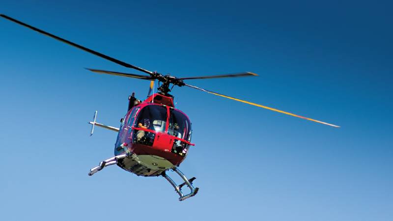 A red helicopter in flight against a blue sky.